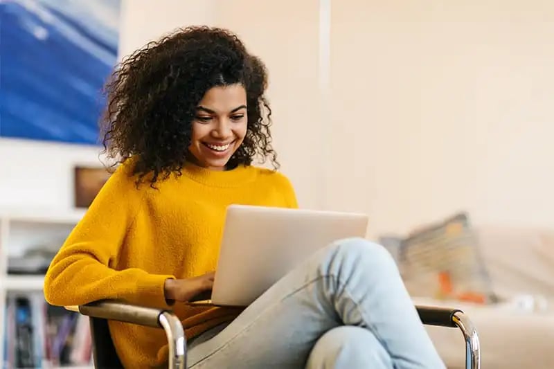 A woman at home on a chair, wanting to play sports looking on her laptop.